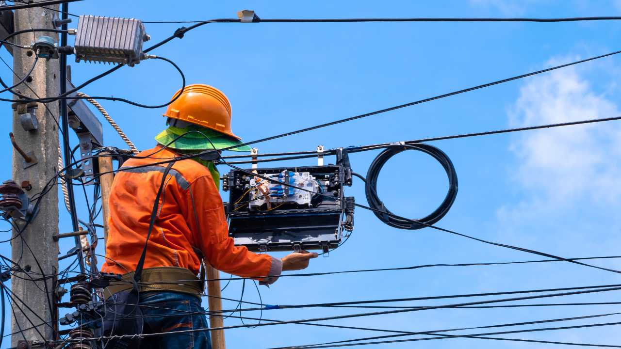 Técnico instalando empalme de fibra óptica en poste de vía pública